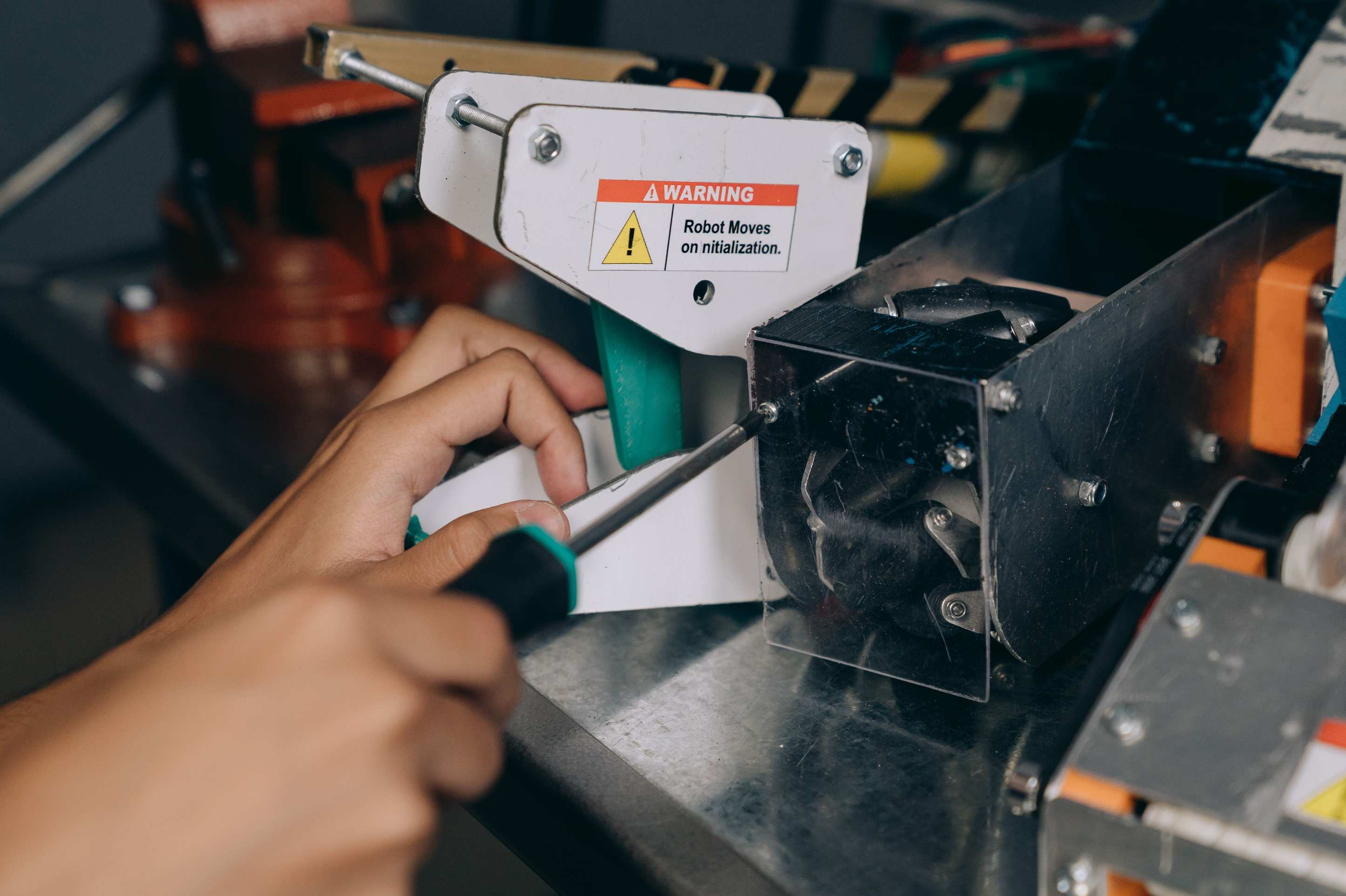 Close-up of a hand using a screwdriver to fix industrial robot machinery indoors